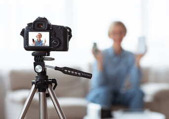 Young Caucasian woman recording video content for her tech blog at home, selective focus on camera with preview screen
