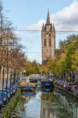 Fototapeta na wymiar Delft, The Netherlands, November 11, 2020: view along Oude Delft canal towards the Old Church on a sunny day in autumn