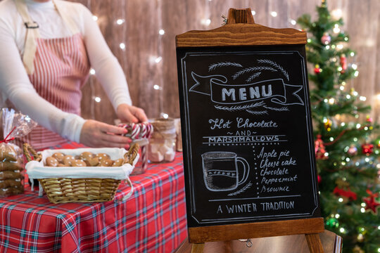 Christmas pastry shop with menu on chalk board. Woman seller, waitress selling sweets  in a small cozy cafe.