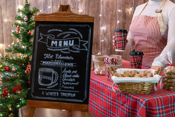 Christmas pastry shop with menu on chalk board. Woman seller, waitress selling sweets and hot chocolate in a small cozy cafe.