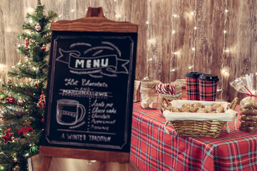 Christmas pastry shop . Woman seller, waitress selling gingerbread, marshmallows, cookies, sweets and hot chocolate in a small cozy cafe. Homemade bakery menu in the foreground