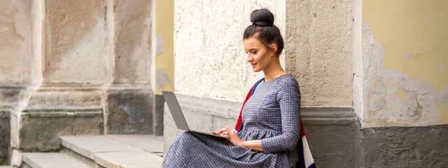 A teenage happy student working on a laptop computer on stairs outdoors