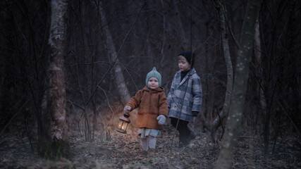 Small children, walk through the night scary autumn or winter forest. The girl carries a lamp with...