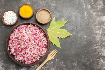 Vegetable salad with various ingredients in a brown bowl and different spices leave and fork on dark background