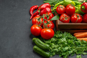 Close up view of vegetable basket with a bunch of green and peppers cucumber and tomatoes with stem carrots beets on dark background stock photo
