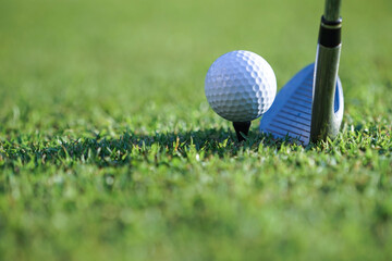 Golf clubs and golf balls on a green lawn in a beautiful golf course with morning sunshine.Close up of golf ball on a tee with the golf clubs ready to hit the ball.