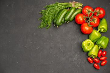Horizontal view of fresh vegetables red tomatoes with stems green peppers and cucumbers a bunch of green necessary for cooking on dark background