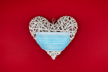White heart with a blue face mask on a red background. Concept of a Valentines day during Coronavirus or Covid pandemic.