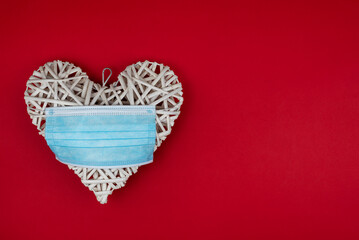 White heart with a blue face mask on a red background. Concept of a Valentine´s day during Coronavirus or Covid pandemic..