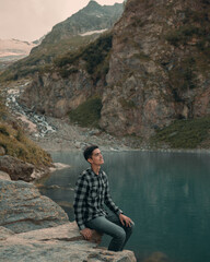 a young guy hiker climbed into the mountains and sat on the shore of a mountain lake