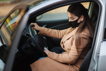 Beautiful young girl in a mask sitting in a car and put on protective gloves. Protective mask against covid-19, driver on a city street during a coronavirus outbreak