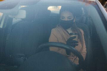 Beautiful young girl in a mask sitting in a car and put on protective gloves. Protective mask...