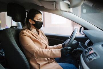 Beautiful young girl in a mask sitting in a car and put on protective gloves. Protective mask...