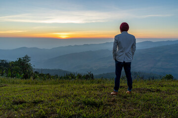 Young man traveler looking at the sunrise over the mountain