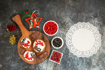 top view berry cakes and chocolates on chopping board xmas toys bowls with pomegranate raisins and...