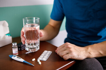 Fototapeta na wymiar Hands man in holding pill and glass of water over table while sitting on couch and going to take medicine