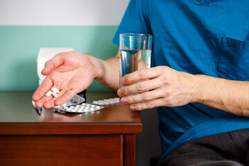 Hands man in holding pill and glass of water over table while sitting on couch and going to take medicine