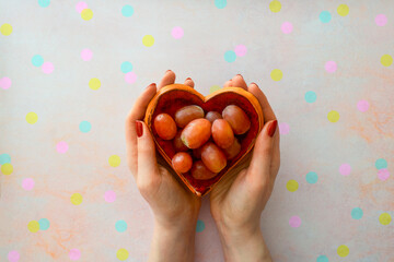 The Twelve Lucky Grapes. Heart bowl held by female hands with grapes eaten one by one with every stroke of the clock on New Year's Eve in Spain on a festive background with confetti. Spanish tradition