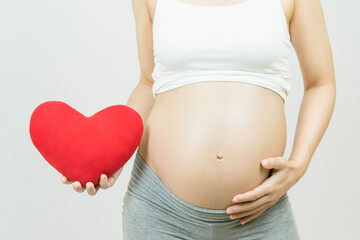 Selective focus of a tummy of a pregnant woman with red heart on hand isolated on gray background, body part, happy pregnancy time, new life concept