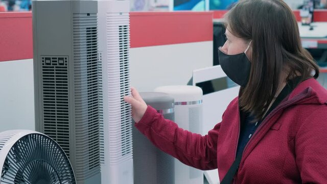 Caucasian a women wearing antivirus medical mask and red jacket picks out convector in electronics shop. Concept of shopping during epidemic, pandemic