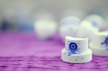 The soiled blue nozzles from the paint sprayer lies on a purple plank on a background of a many...