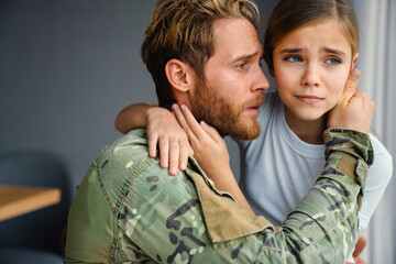Masculine military man hugging her crying daughter while kneeling - obrazy, fototapety, plakaty
