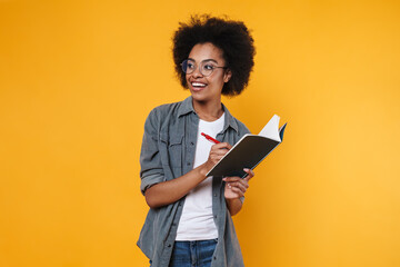 Joyful african american girl in eyeglasses writing in exercise book