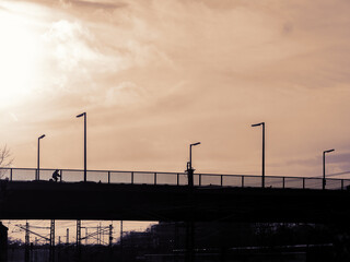 Fototapeta na wymiar Silhouette of A Bridge With An Unidentifiable Cyclist Against A Sunny Cloudy Sky
