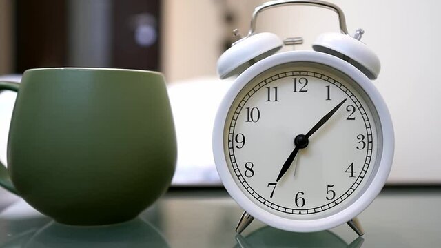 Alarm clock and a cup of hot coffee on the table in the bedroom. The clock rings and wakes us up early in the morning. It's time to wake up and go to work. Wake up early and start a wonderful new day