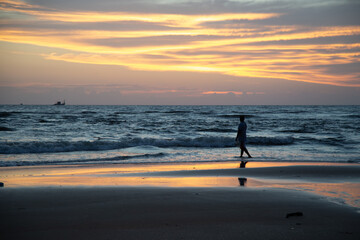 Silhouette of a man walking along the beach in sunset time