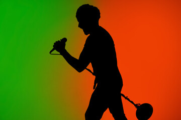 Stage. Silhouette of young male guitarist isolated on green-orange gradient studio background in neon. Beautiful shadow in action, performing. Concept of human emotions, expression, ad, music, art.