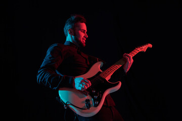 Obraz premium Inspired. Silhouette of young male guitarist isolated on blue-pink gradient studio background in neon. Beautiful shadow in action, performing. Concept of human emotions, expression, ad, music, art.