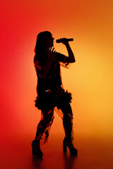 Talented. Silhouette of young female singer isolated on orange gradient studio background in neon light. Beautiful shadow in action, performing. Concept of human emotions, expression, ad, music, art.