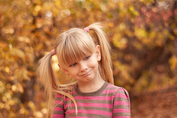Fototapeta premium Cute little girl in the autumn park. The child smiles. Portrait of a blonde-haired blue-eyed girl.