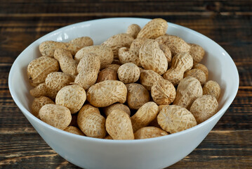 Peanuts in a white bowl on an old shabby board. Nuts on a brown wooden table.