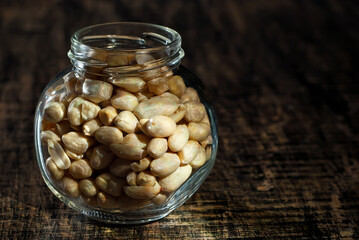 Peanuts in a glass transparent jar. Nuts on an old shabby board. Jar on a brown wooden table close...