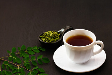 moringa tea in white cup ceramic and moringa leaf on black wooden background