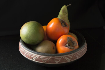 Fototapeta na wymiar Pears, Kaki fruit and a Mango in a bowl with black background