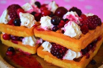 Close-up of a waffle filled with cream, cherries and berries on a pink cloth with white dots