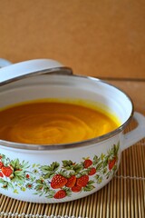 Pumpkin and carrot soup in white pot on wooden background