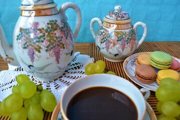 Porcelain set including a cup of tea and a plate of macarons surrounded by grapes on a wooden table