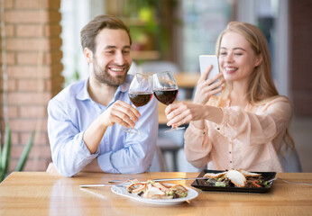 Portrait of lovely lady taking picture of toast with clinking wine glasses during holiday dinner at restaurant