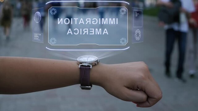 Female hand with futuristic smartwatch interacts HUD hologram with text Immigration America. Woman uses holographic technology on wristwatch against the background of evening city with people