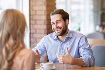Happy young guy talking to his girlfriend while having coffee at cafe. Lifestyles and relationships concept