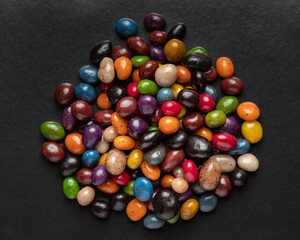 Fototapeta na wymiar A heap of multi-colored glazed raisins on a black background. Rounded candies of different colors and sizes. Healthy and tasty snack.