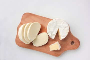 Sliced mozzarella cheese and camembert on cutting board on white table. Overhead view