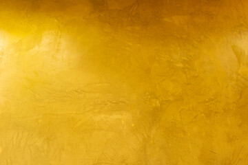 Gold wall texture background. Grunge yellow shiny gold foil paint on wall surface with light reflection, vibrant golden luxury wallpaper
