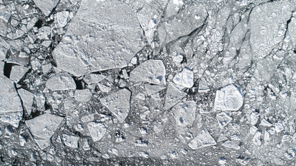 Aerial view over the surface of water and cracked ice. Stunning abstract view of sea ice.
