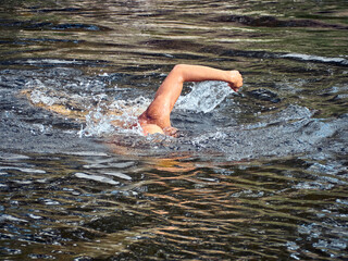 Man swims freestyle in open water on the river in summer