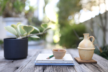 Tea in clay cup and ewer with plant and notebook
